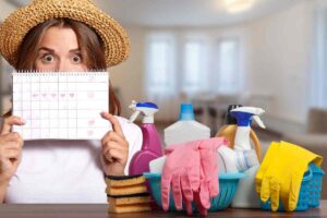 Una donna con un cappello di paglia tiene un calendario decorato, circondata da prodotti per la pulizia.